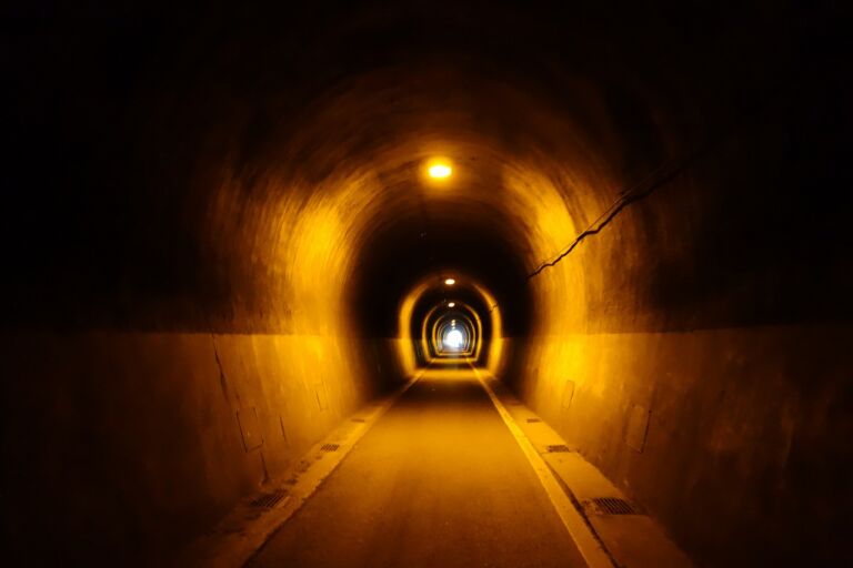 A dark tunnel with lights inside, leading to a bright light at the end.